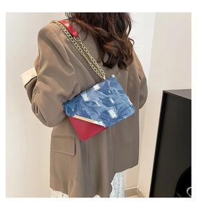 Detail of contrast blue denim and red leather crossbody bag with golden chain strap