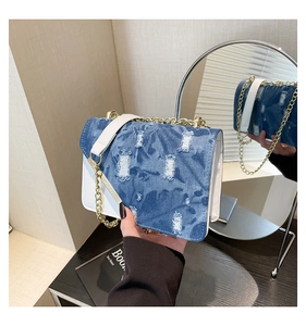 Detail of distressed blue denim flap and white leather trim on a stylish shoulder bag