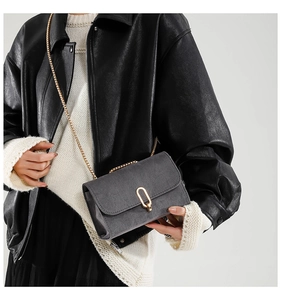 Close-up of grey suede crossbody bag with gold chain strap and U-shaped metal buckle