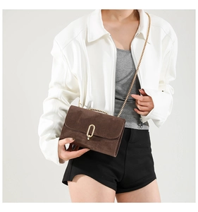 Detail of a dark brown suede crossbody bag with gold oval lock and elegant chain strap