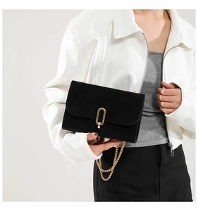 Detailed view of the golden metal clasp and chain strap on a black matte flap bag