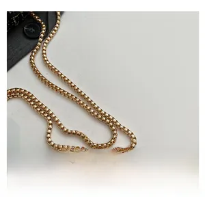 Macro shot of polished gold box chain strap on a dark grey tailored suit jacket