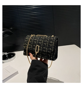 Gros plan sur la texture en tweed noir et doré avec boucle ovale et bandoulière chaîne