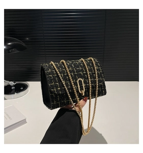 Close-up of black and gold tweed texture with metallic chain on a stylish shoulder bag