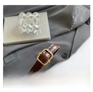 Detail of adjustable dark brown faux leather shoulder strap with a golden metal buckle