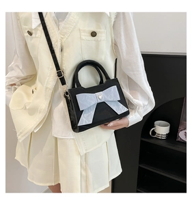 Detail of a black handbag featuring a large light blue bow and a heart-shaped metal accent