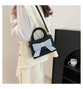 Detail view of a black patent leather handbag featuring a large light blue bow and heart crystal