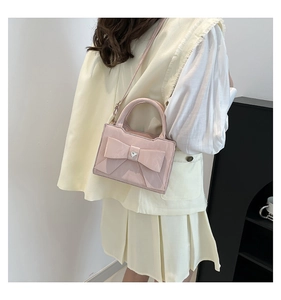 Pink bow handbag with heart-shaped rhinestone being worn as a crossbody bag by a model
