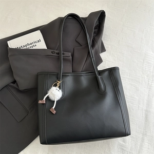 Dettaglio della borsa tote in pelle nera opaca con ciondolo in peluche bianco e cuciture
