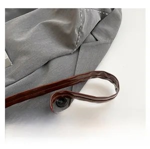 Close-up of grey textured shoulder bag featuring white decorative stitching and brown strap