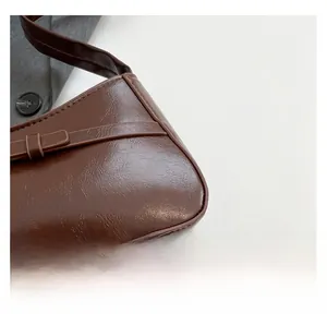 Close-up of brown glossy PU leather texture and decorative buckle on shoulder bag