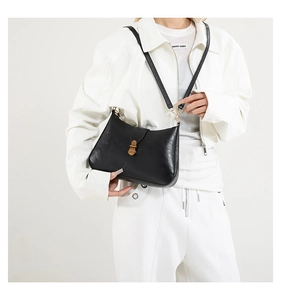 Detail of vintage black leather shoulder bag with a polished gold buckle on a white outfit