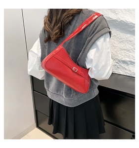Detail view of red glossy shoulder bag with silver buckle worn by a model in a modern room