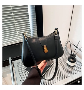 Close-up of a black glossy leather underarm bag featuring a vintage gold metal clasp
