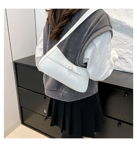 White minimalist leather baguette shoulder bag shown being worn by a model from the side
