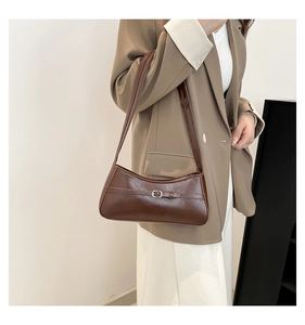 Close-up of a brown baguette bag with a silver buckle worn by a model in a beige suit
