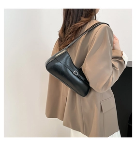 Detailed view of black glossy leather underarm bag with buckle detail on a model