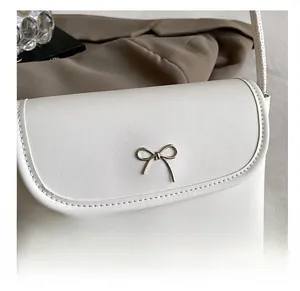 Close-up of a white leather underarm bag with a decorative gold metal bow on the flap
