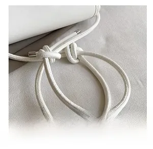Detail show of white leather shoulder bag featuring hand-knotted rope strap and metal tips