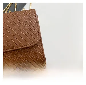 Detail shot of brown embossed leather texture and gold metal chain on small crossbody bag