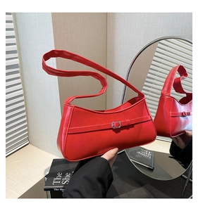 Close-up of a red leather underarm bag featuring a metallic buckle and slim shoulder strap