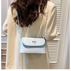 Close-up of a light blue crossbody bag featuring a decorative gold metal bow detail