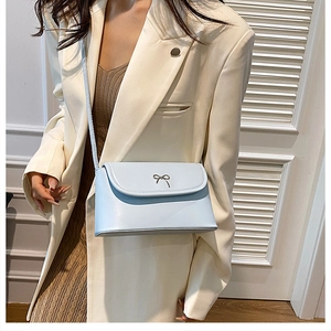 Detail of light blue crossbody bag with metal bow on light-colored suit outfit
