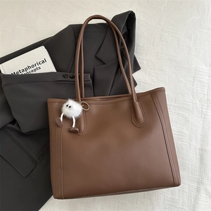 Dettaglio della borsa tote in ecopelle marrone con ciondolo mostro di peluche bianco su tessuto