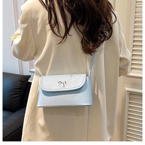 Detail of light blue crossbody bag with silver bow buckle worn on a white blazer