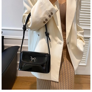 Fashionable black patent leather shoulder bag with a silver bow knot shown on a model