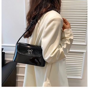 Detail of glossy black patent leather bag with a delicate silver bow on white blazer