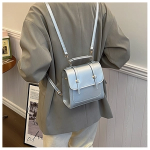 Detail of silver metallic leather backpack with buckle straps worn over a grey blazer