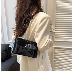 Detail of a black patent leather shoulder bag with a silver bow buckle on white blazer