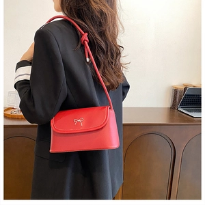 Close-up of red underarm bag with silver bow buckle and knotted strap on black blazer