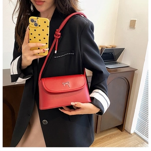 Detail of red leather crossbody bag with silver bow and stylish knotted shoulder strap