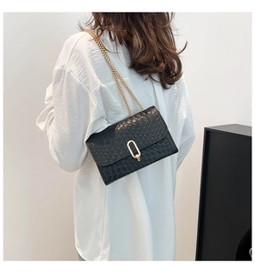 Detail of black textured crossbody bag with gold chain strap and U-shaped buckle on model