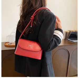 Detail of red small square bag with silver metal bow and knotted shoulder strap