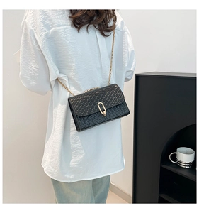 Détail d'un sac bandoulière tressé noir avec chaîne dorée et fermoir métallique sur modèle