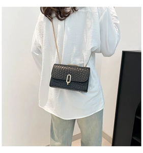 Detail of black woven texture handbag with golden chain and oval metal clasp on a model