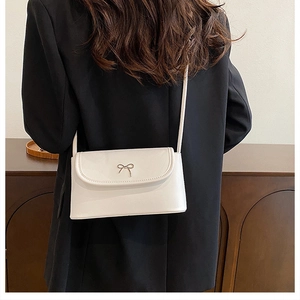 Detailed back view of a white minimalist square bag with golden bow hardware on model