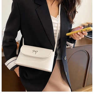Detail of white leather crossbody bag featuring a silver metal bow on a black suit model