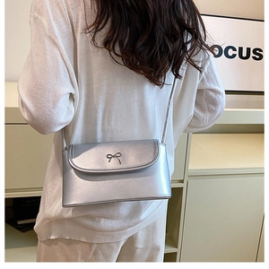Detail view of silver crossbody bag with metallic finish and bow accent on a model