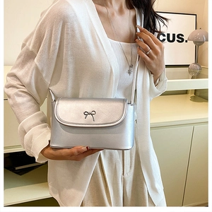 Detail of silver metallic crossbody bag featuring a delicate metal bow clasp decoration