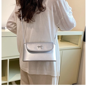 Silver shoulder bag with metallic bow detail shown on a model for size reference