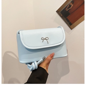 Close-up of light blue flap bag with silver metal bow and thick rope braided strap