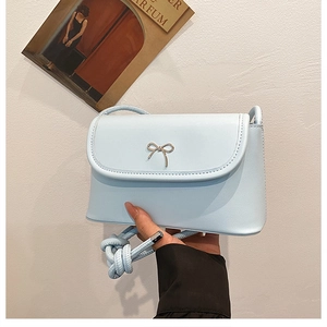 Close-up of light blue crossbody bag featuring a golden metal bow and rope strap