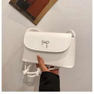 Handheld view of a mini white leather crossbody bag with a silver metal bow detail
