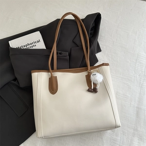 Dettaglio di una borsa tote minimalista in ecopelle beige con finiture marroni e ciondolo