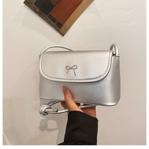 Detail of silver crossbody square bag featuring a metallic bow and flap closure