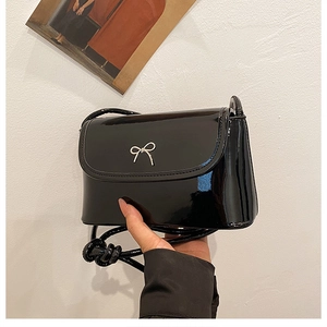 Close-up of black patent leather crossbody bag with silver metal bow detail